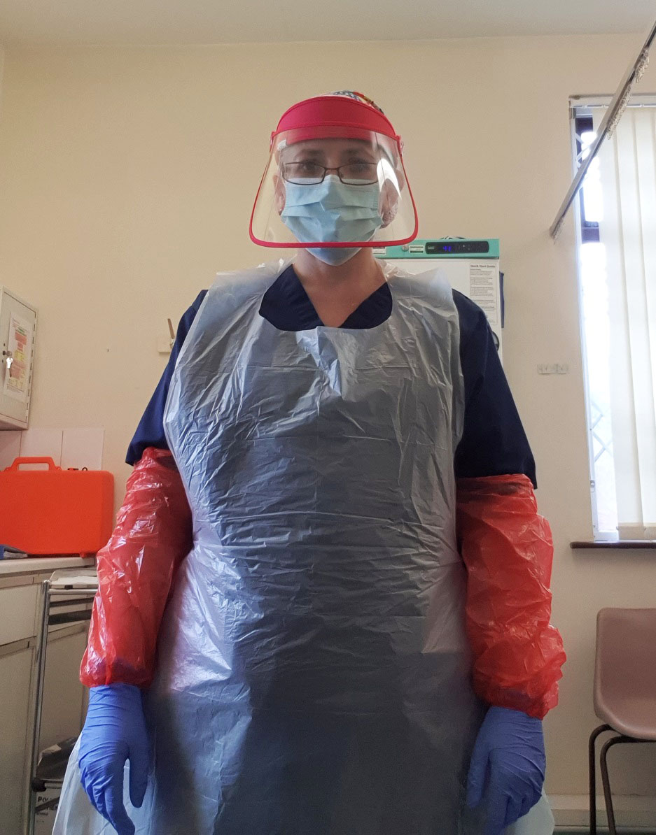 A nurse dressed in full personal protective equipment, or PPE, including a mask, face visor, gloves, plastic sleeves and a plastic apron.